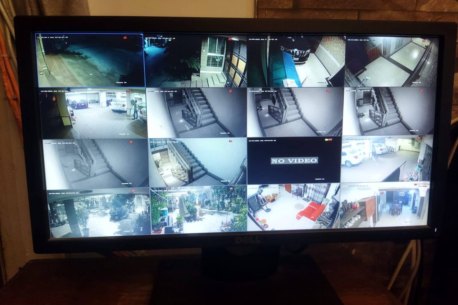 A Dell monitor displaying a multi-channel CCTV surveillance grid of 16 camera feeds from a property installation, with diverse views including parking, staircases, an courtyard, and an interior room.