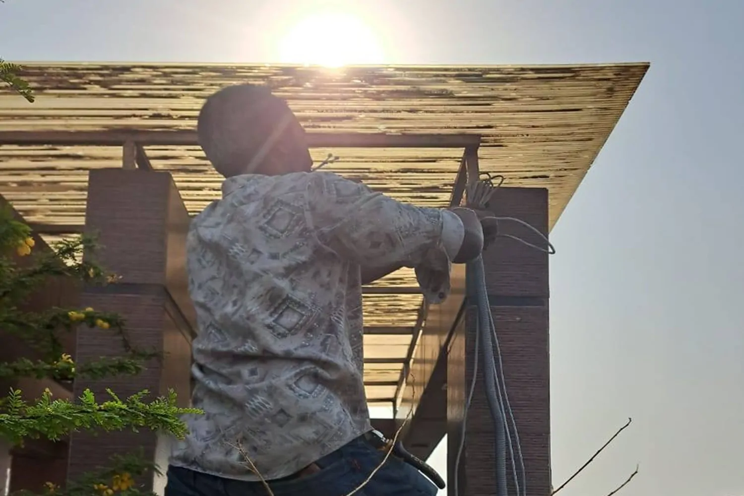 A technician standing on a ladder, using a screwdriver to securely mount a white dome-style CCTV camera to an exterior building wall.